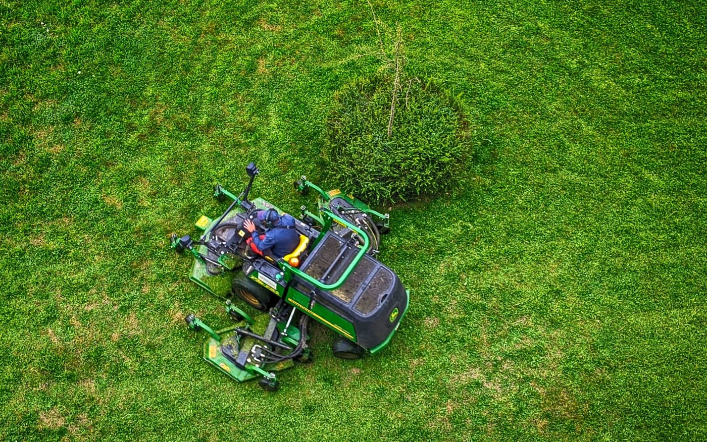 An aerial view of a wide-deck mower cutting an open green lawn